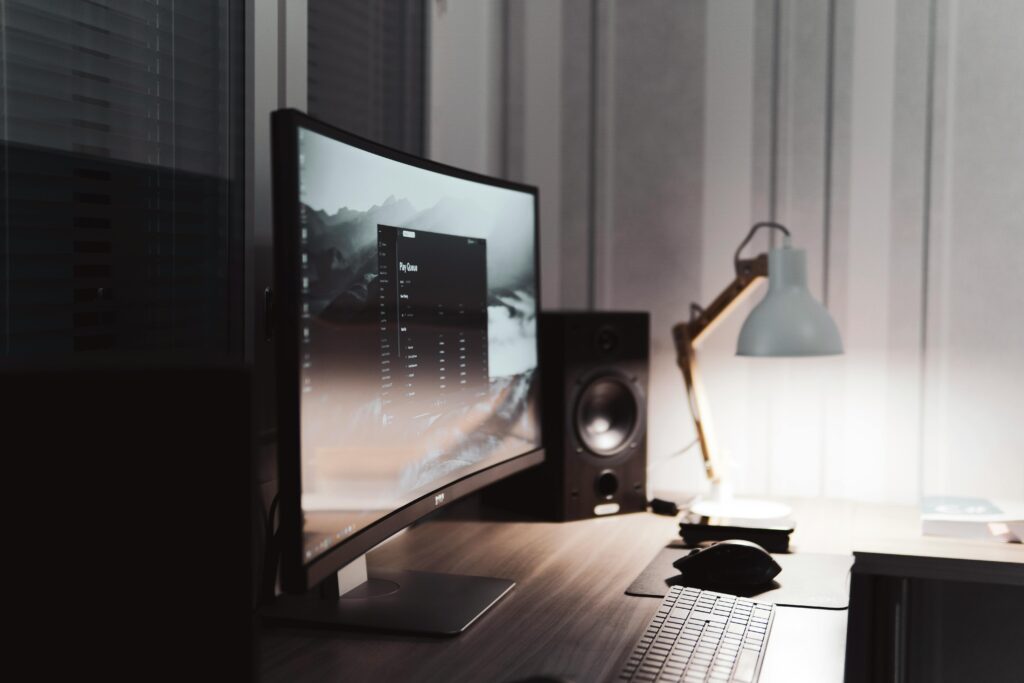 Contemporary office setup with a curved monitor and stylish lamp on a wooden desk.